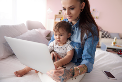 Image of mother working at laptop on bed at home, with small child on lap
